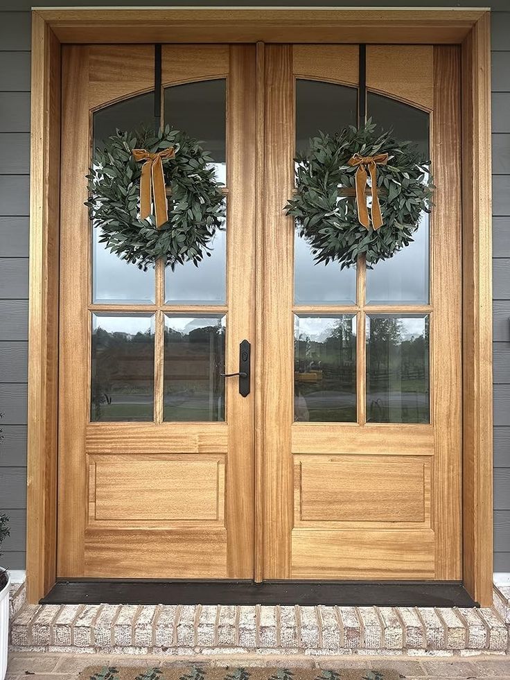 two wreaths on the front door of a house with windows and sidelights,