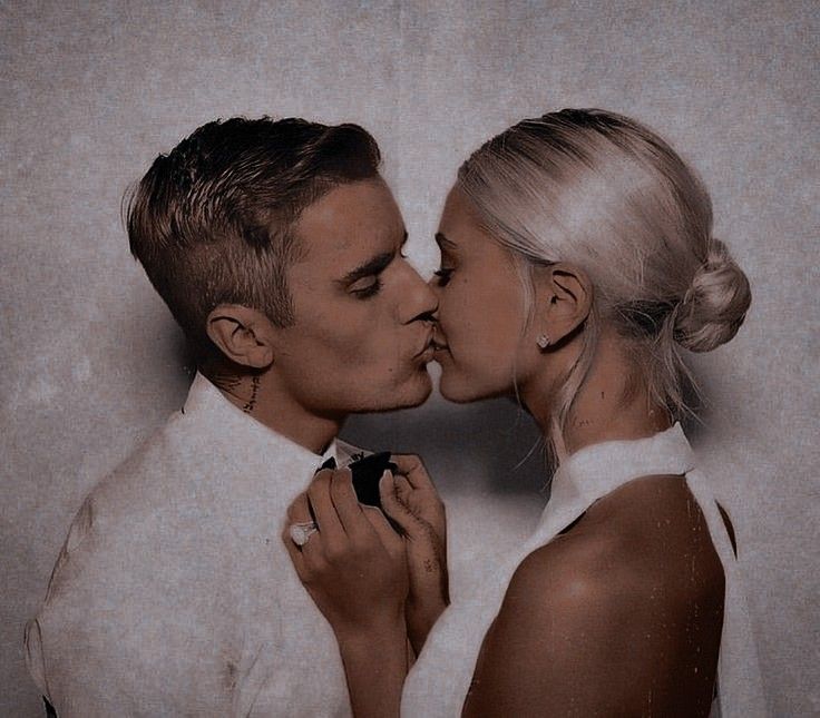 a man and woman kissing each other in front of a white wall