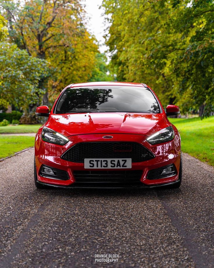 a red car parked on the side of a road next to some grass and trees