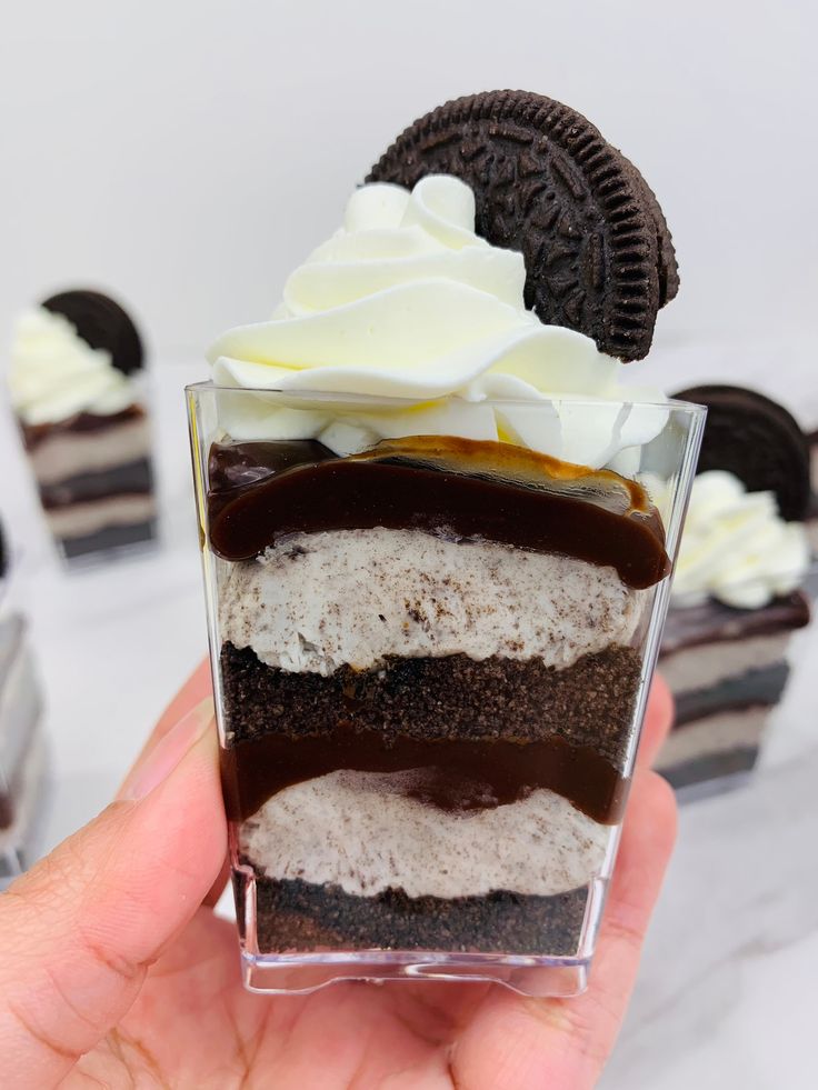 a hand holding a chocolate dessert with white frosting and oreo cookies on top