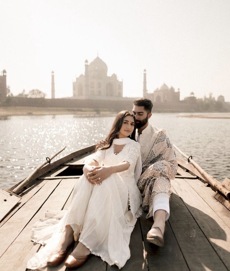 a man and woman are sitting on a boat in front of a body of water