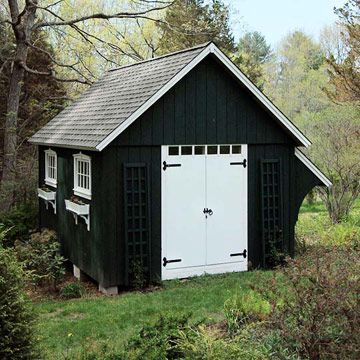 a small black and white shed in the middle of some grass with trees around it