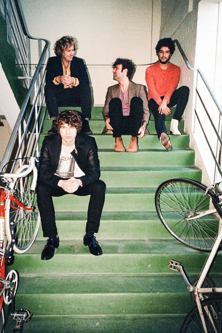 four men sitting on the stairs with their bikes in front of them and one man standing next to his bike