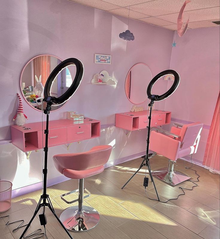 two pink chairs in front of mirrors with lights on them