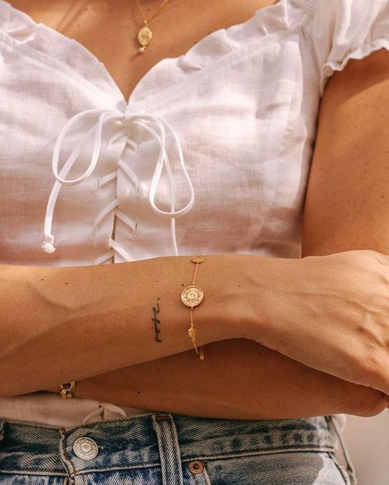 a woman's arm with a cross on it and a coin bracelet attached to the wrist