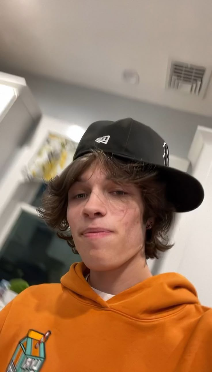 a boy wearing an orange hoodie and black hat