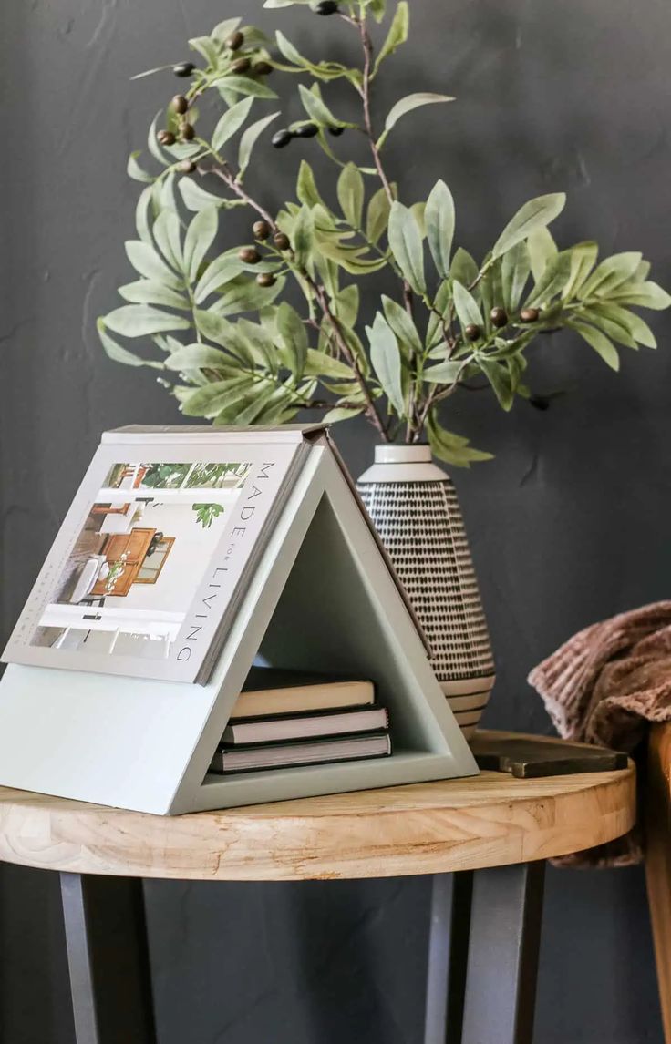 a wooden table topped with a vase filled with green leaves and a photo frame sitting on top of it