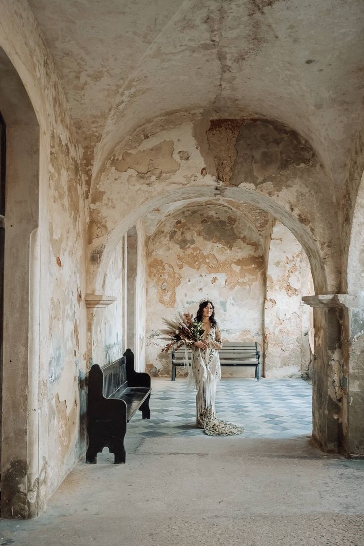 a woman is standing in an old building with a piano and flowers on the bench