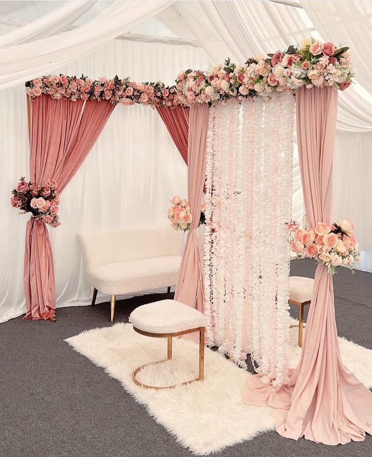 a white and pink wedding setup with draping, flowers, and candles on the floor