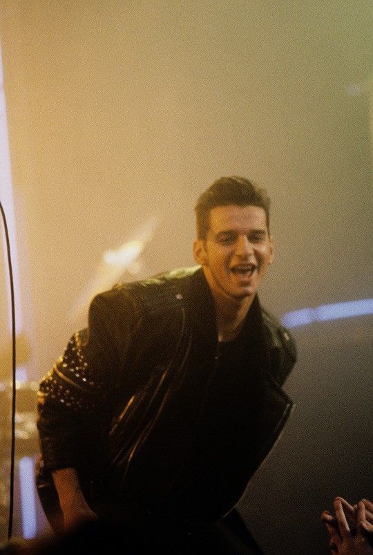 a man standing in front of a microphone and wearing a leather jacket with studded sleeves