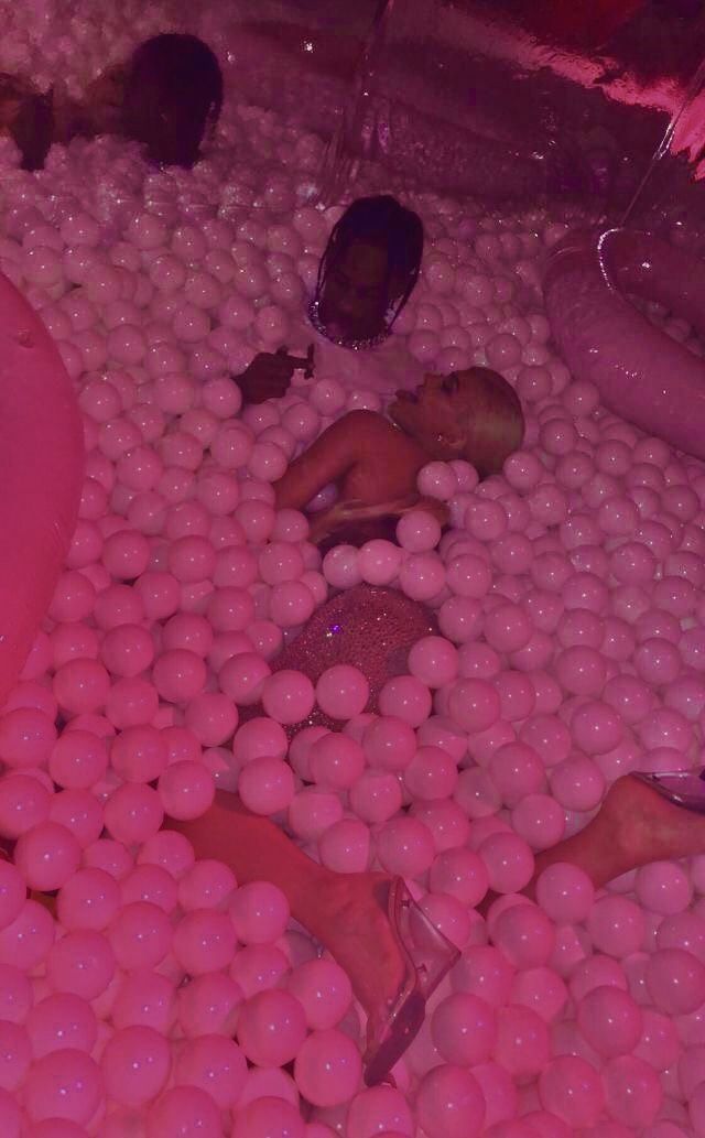 some people are laying down in a ball pit with pink balls on the floor and one person has fallen asleep