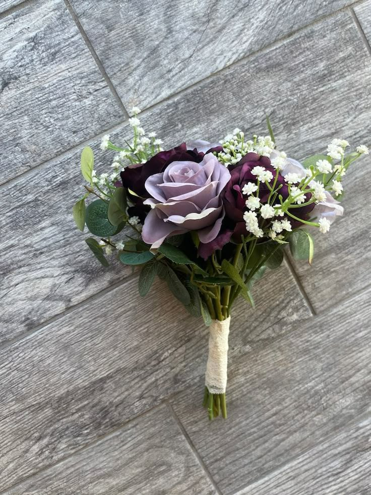 a bridal bouquet with purple flowers and baby's breath on a wooden floor