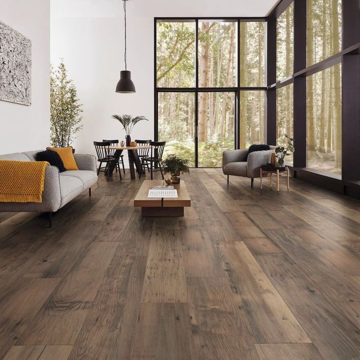 a living room with wood flooring and large windows in the back ground, surrounded by furniture