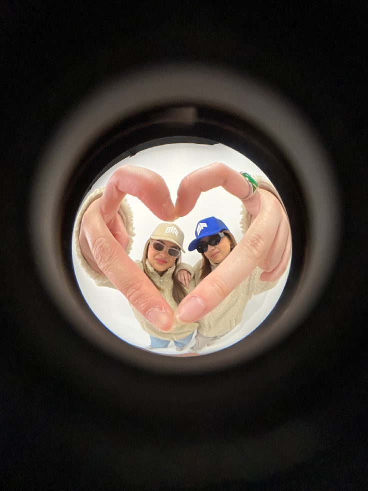 two people making a heart shape with their hands while standing in front of the camera