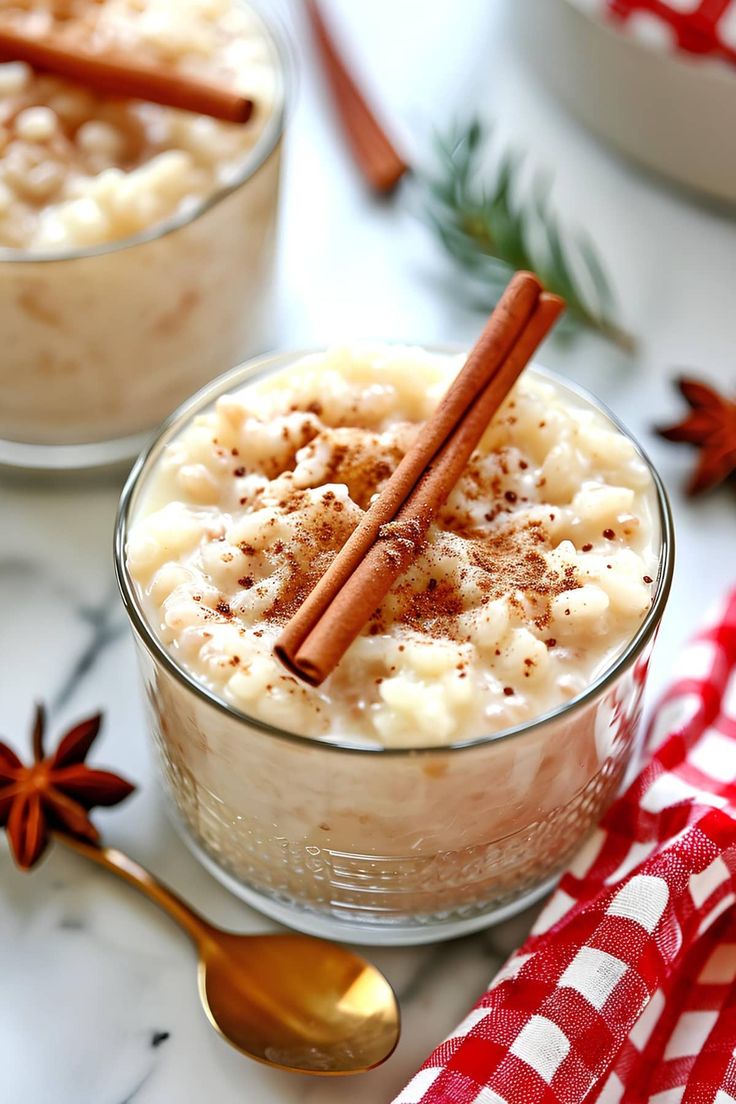 two desserts with cinnamon sticks in them on a white tablecloth and red checkered napkin