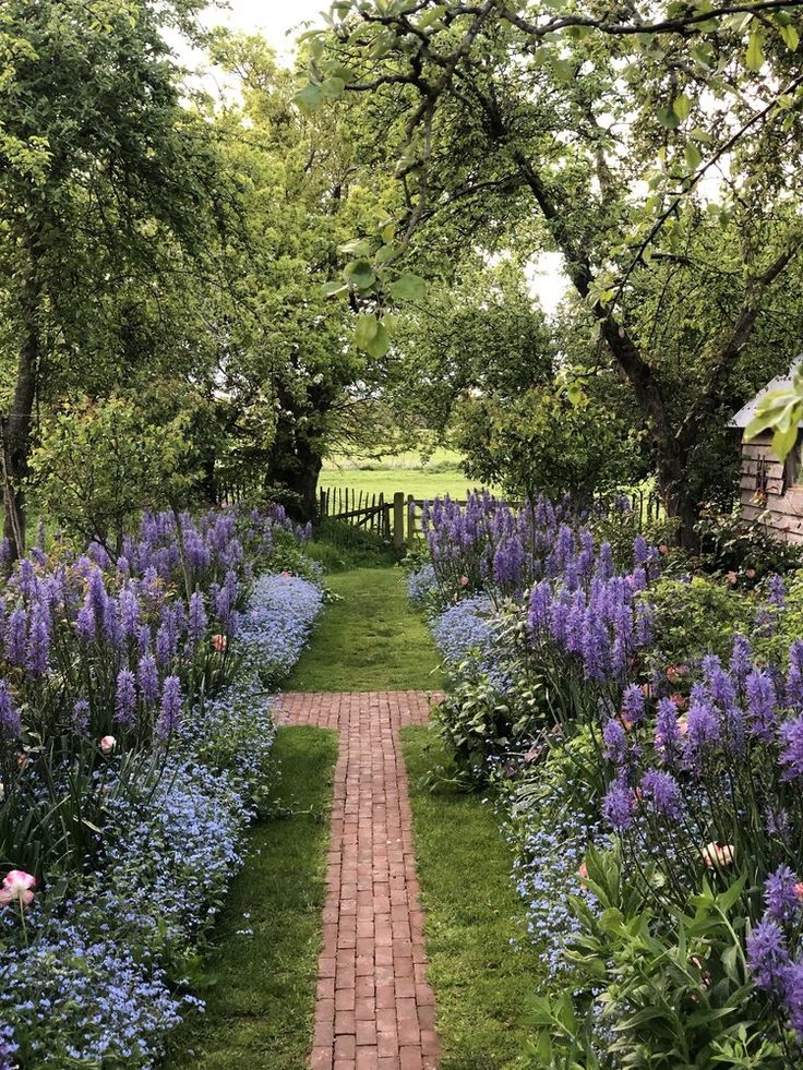 a brick path in the middle of a garden with blue and purple flowers on both sides