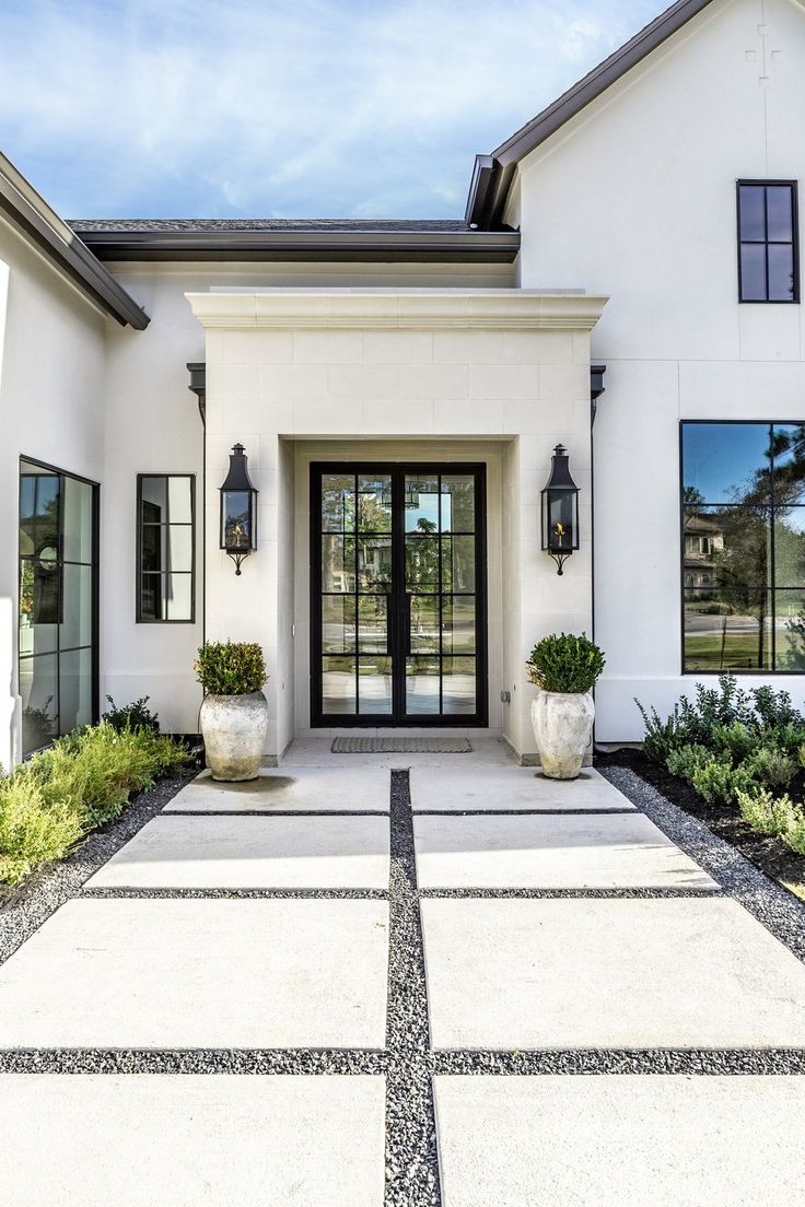 a white house with black doors and two planters on the front door, surrounded by grass