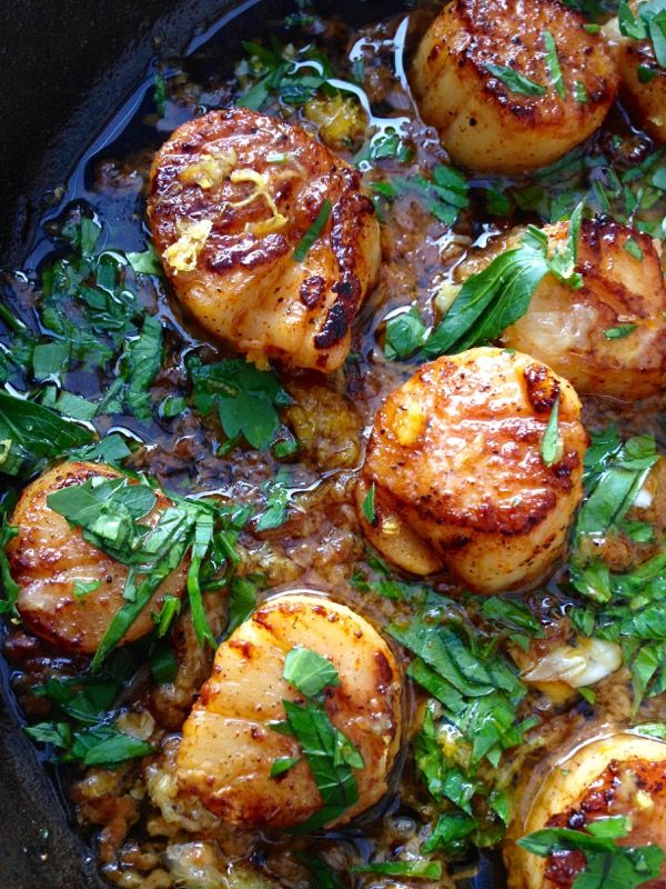 some food is cooking in a pan with sauce and greens on top, including scallops