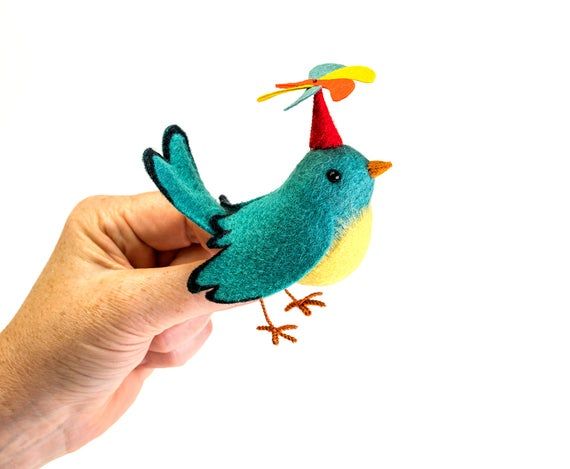 a hand holding a small felt bird with a party hat on it's head