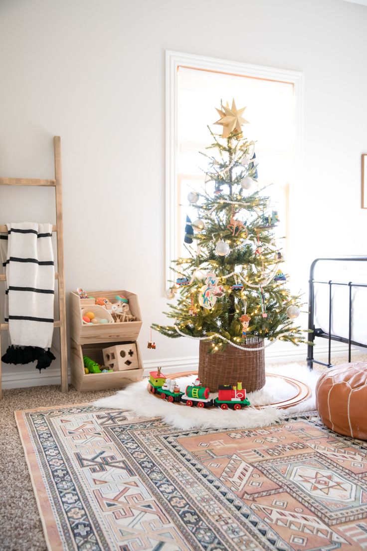 a small christmas tree sitting in the corner of a room next to a bed and rug