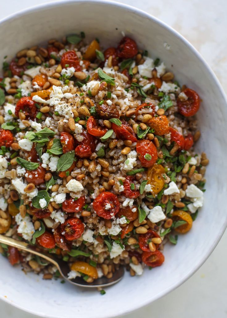 a white bowl filled with grains, tomatoes and feta cheese