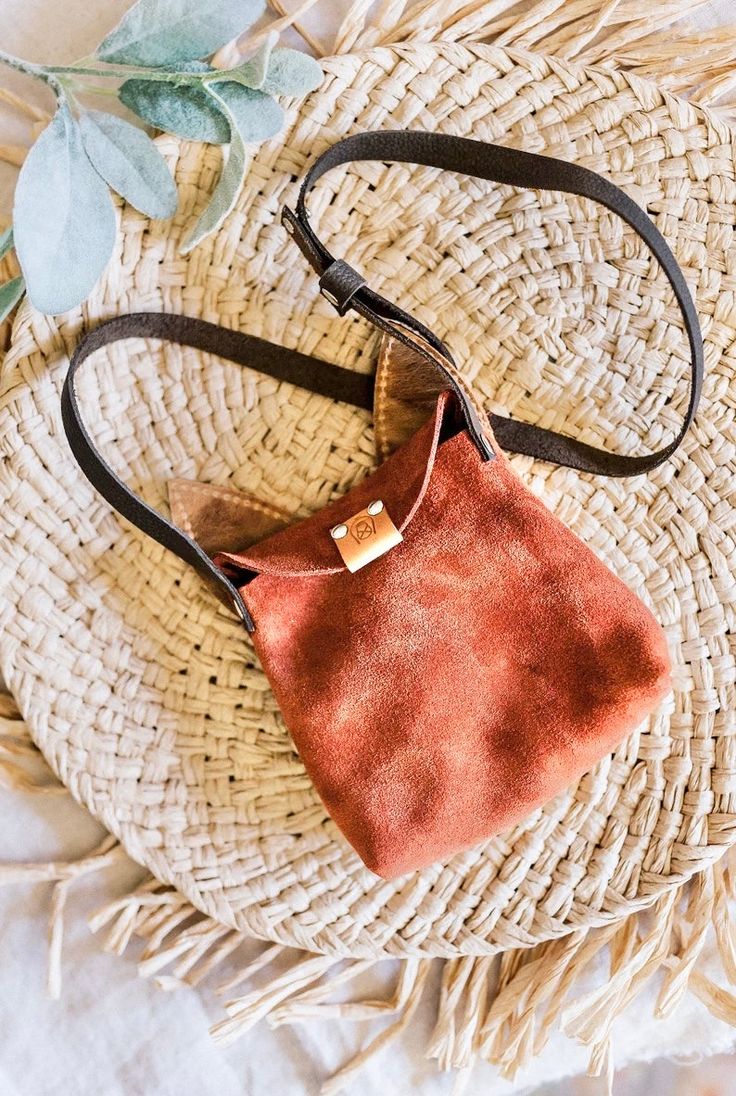 an orange suede purse sitting on top of a wicker basket next to a plant