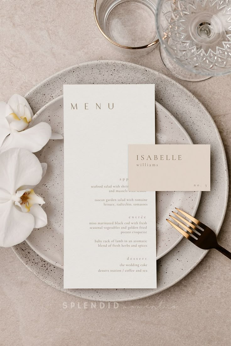 a table setting with white flowers and silverware on it, including a menu card