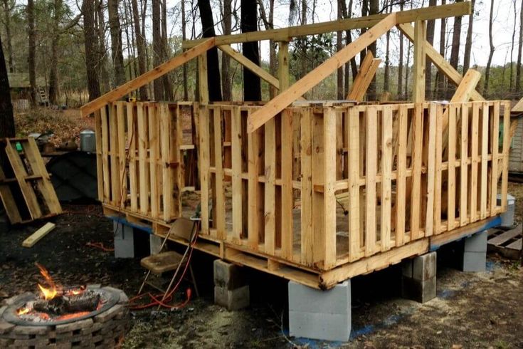 a wooden structure sitting in the woods next to a fire pit with logs around it