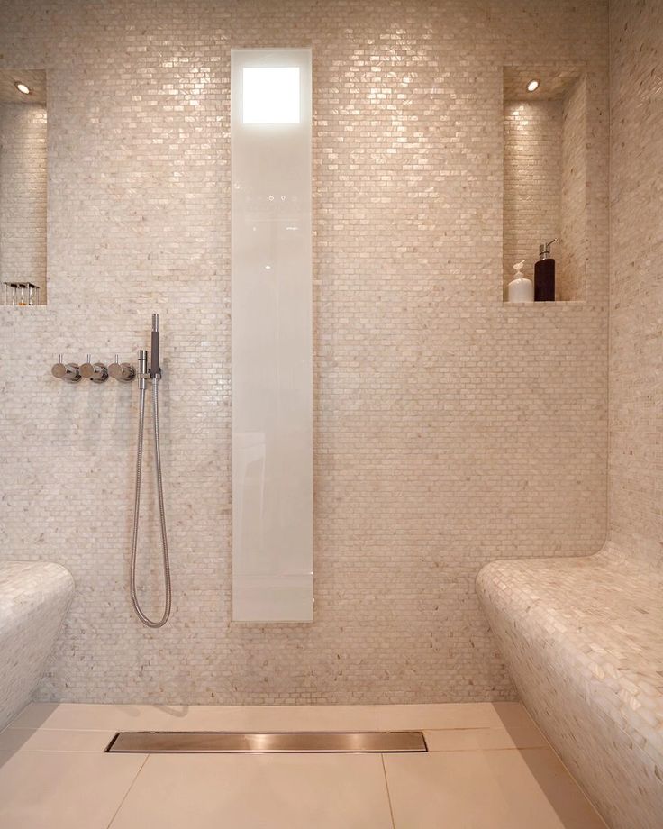 a white tiled bathroom with two sinks and a shower head mounted to the side of the wall