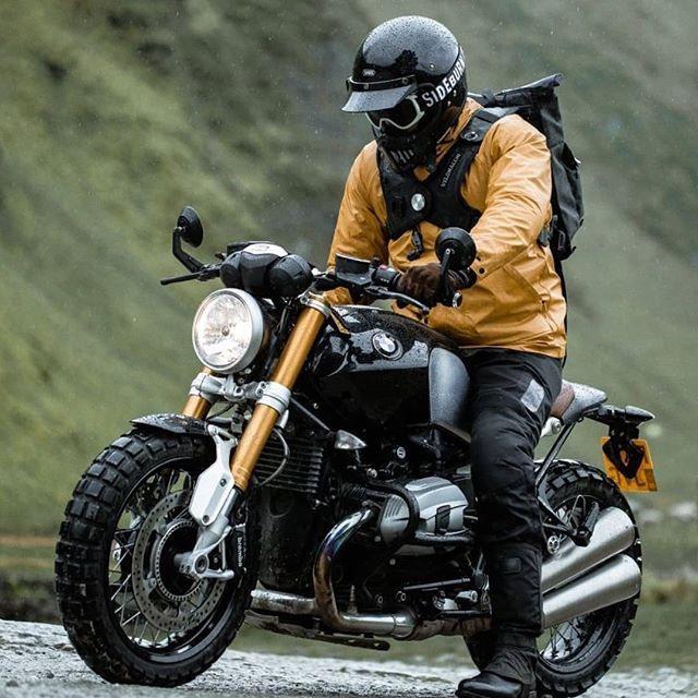 a man riding on the back of a motorcycle down a mountain road in the rain