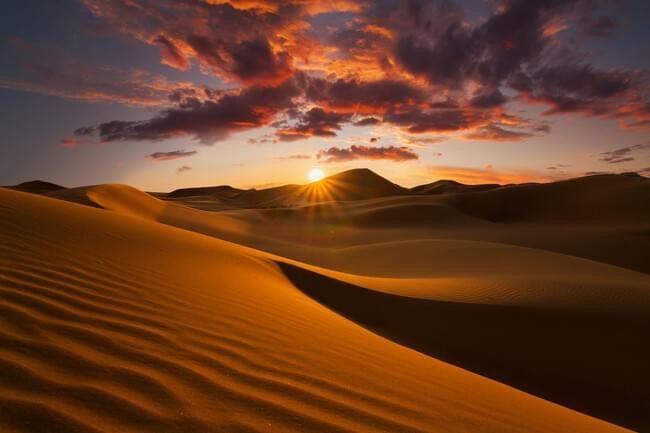 the sun is setting over sand dunes in the desert