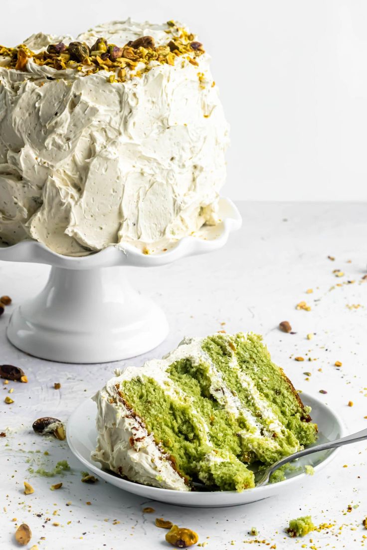 a white cake with green frosting and nuts on top, next to a piece of cake