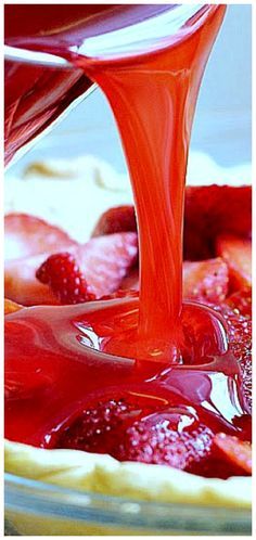 strawberry syrup being poured into a bowl of fruit