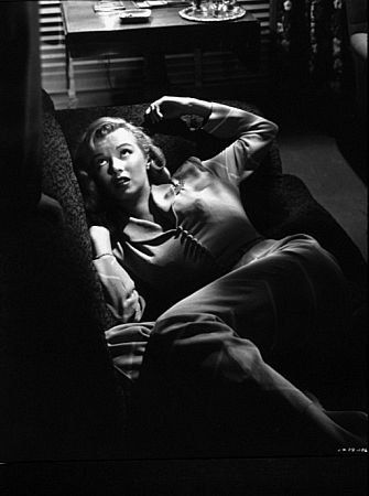 a black and white photo of a woman laying on a couch with her hands behind her head