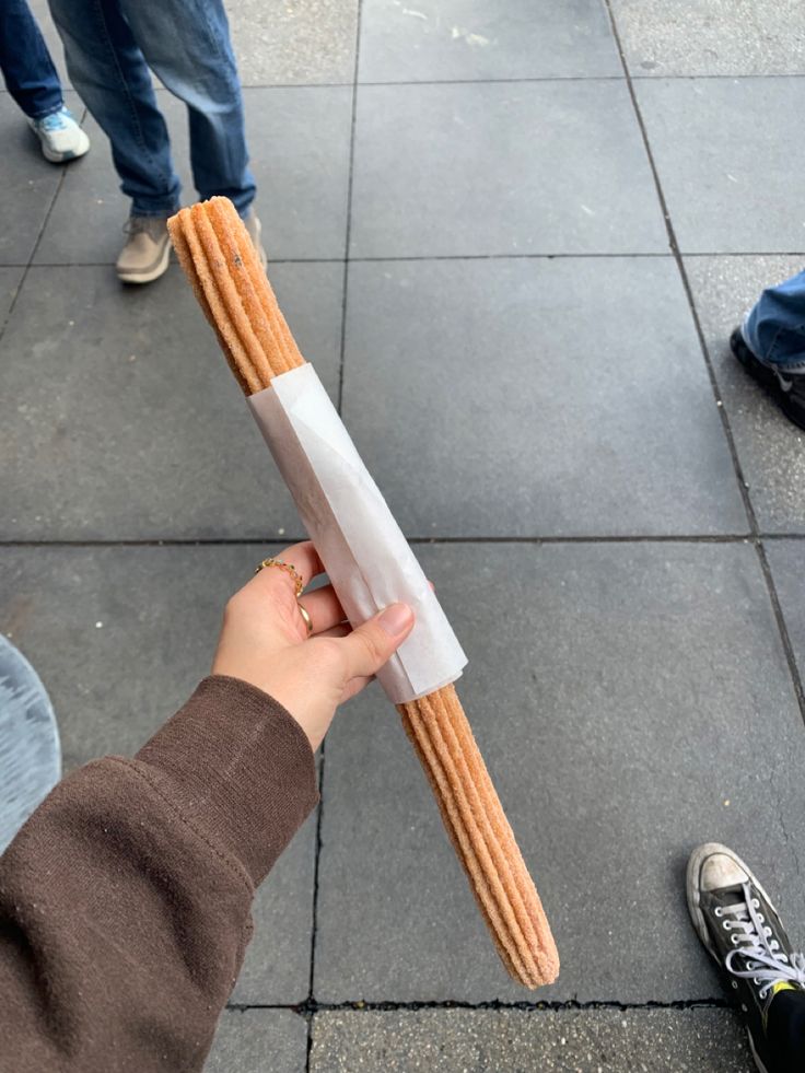 a person holding up a large piece of bread on the sidewalk with other people standing around