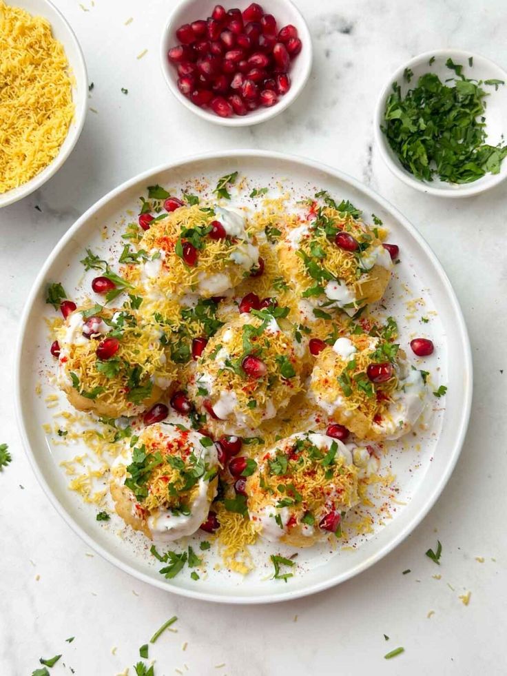 a white plate topped with food next to bowls of rice and pomegranates