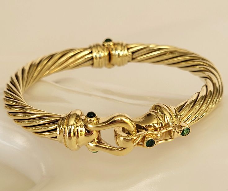 Indulge in the timeless elegance of the David Yurman 14K Yellow Gold Emerald Buckle Cable Bangle Bracelet. Impeccably fashioned from solid 14k yellow gold, this bracelet stands as a testament to meticulous craftsmanship. The design centers around a captivating buckle motif adorned with 2 round faceted green emeralds and 2 round emerald cabochons on both the buckle and hinge, creating a symphony of color and sophistication. The inner circumference of the bracelet is 6.5", the twisted cable is 7mm Bracelet Stands, Bracelet Box, Buckle Bracelet, The David, David Yurman, Chain Link Bracelet, Bangle Bracelet, Chain Link, Timeless Elegance