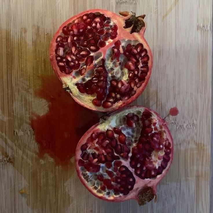 two pomegranates cut in half on a cutting board with brown paint