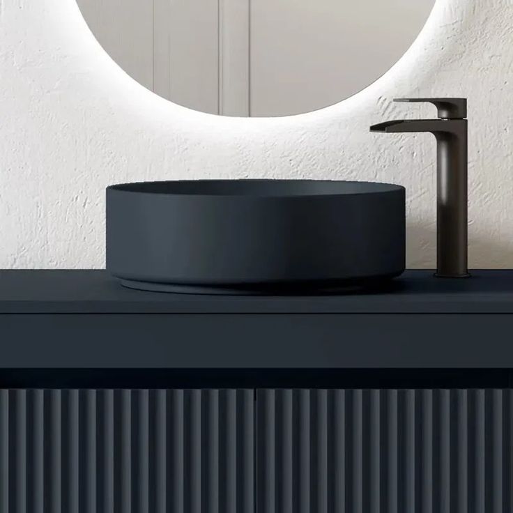 a bathroom sink sitting under a round mirror next to a wall mounted faucet