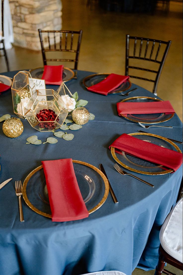 a blue table cloth with red napkins and place settings is set for a formal dinner