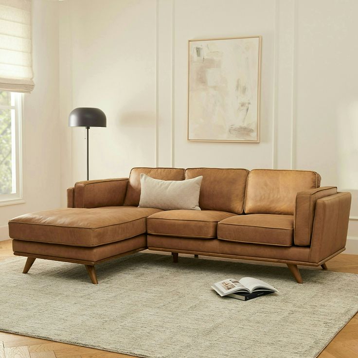 a living room with a brown leather couch and book on the floor in front of it