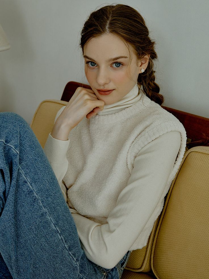 a young woman sitting on top of a couch next to a white wall and wearing blue jeans