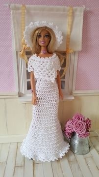 a doll in a white crocheted dress and hat next to a flower pot