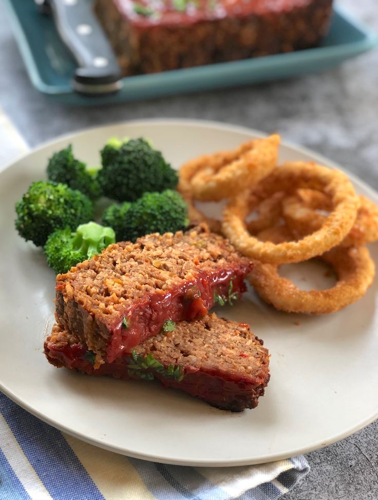 a white plate topped with meatloaf next to broccoli and onion rings