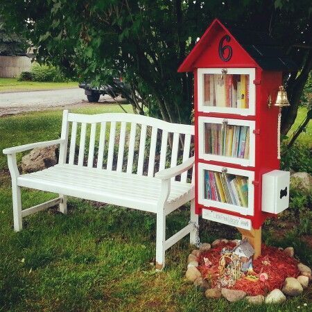 a white bench sitting next to a red book shelf on top of a grass covered field