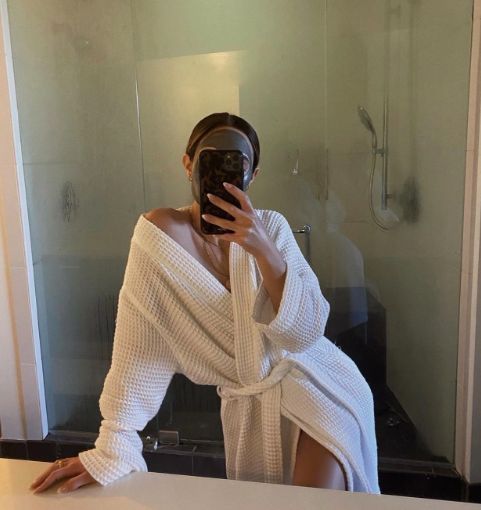 a woman taking a selfie in front of a bathroom mirror while wearing a white robe