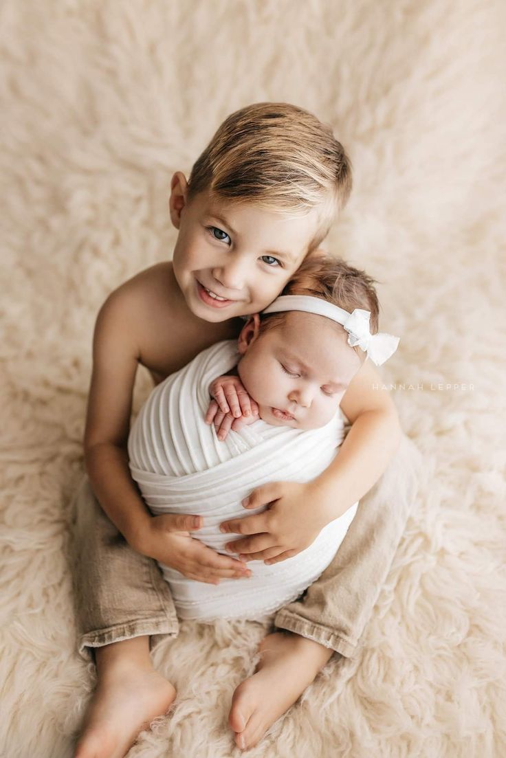 two young children are hugging each other while sitting on a fluffy white blanket in the studio