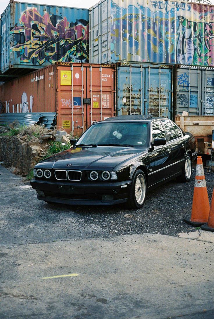 a black car is parked in front of some shipping containers and orange traffic cones