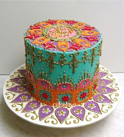 a brightly colored cake on a plate with decorative designs and gold trimmings, sitting on a table