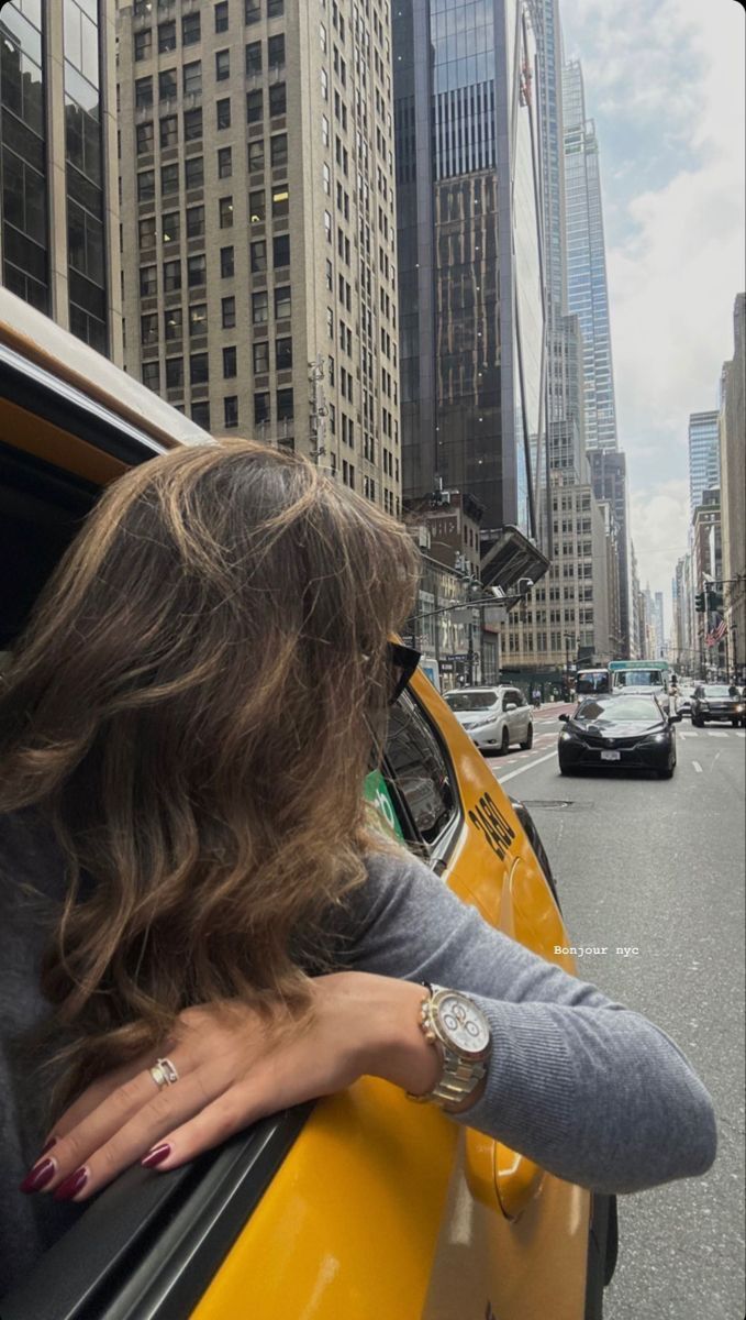 a woman leaning out the window of a taxi cab on a city street with skyscrapers in the background